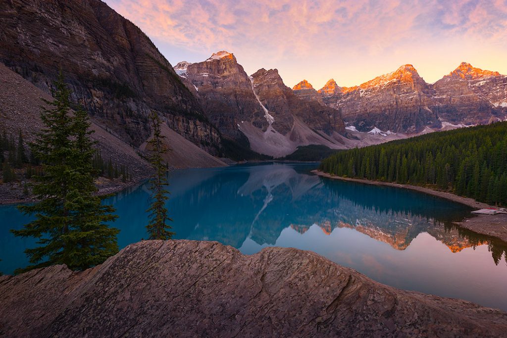 An image of Moraine Lake, Alberta. Taken in the morning at sunrise with the sun hitting the mountain peaks. A nature photography print by Bryce Mironuck